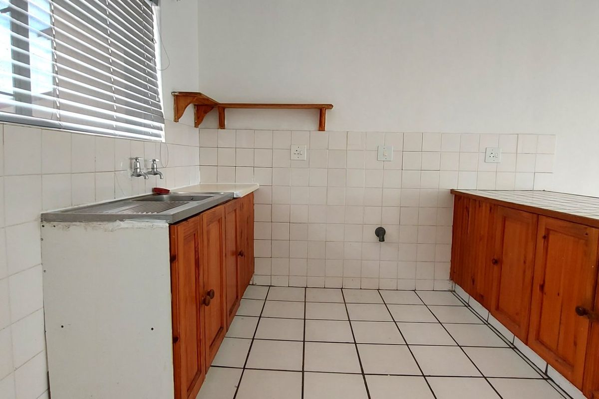 A dated kitchen featuring wooden cabinetry, tiled splashbacks, and tiled flooring, offering a functional space ready for modernization and renovation.