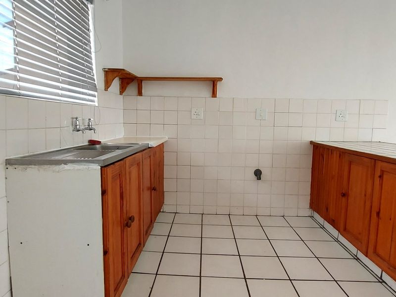 A dated kitchen featuring wooden cabinetry, tiled splashbacks, and tiled flooring, offering a functional space ready for modernization and renovation.