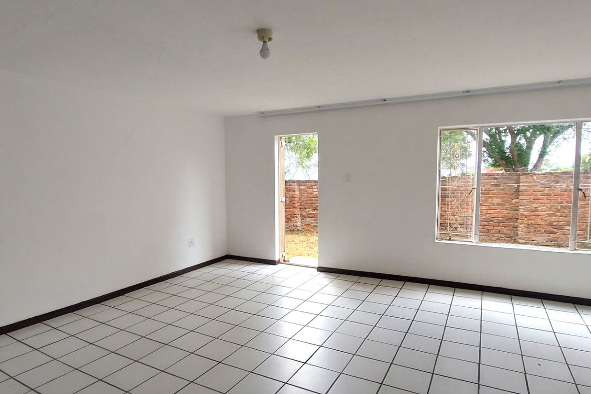 An empty, open-plan living area featuring white walls, ceramic tiled flooring, and direct access to an outdoor space through a security door.