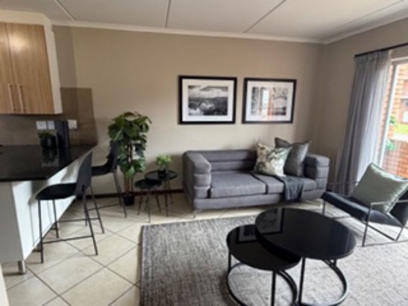 Open-plan living area featuring a modern kitchen with granite countertops and tiled flooring, seamlessly flowing into a comfortable lounge space with balcony access.