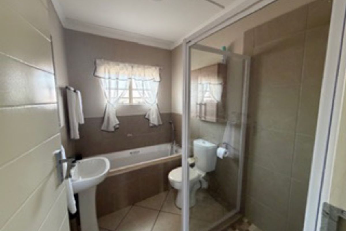 A functional bathroom featuring a pedestal basin, bathtub, and a separate shower enclosure with tiled finishes throughout.