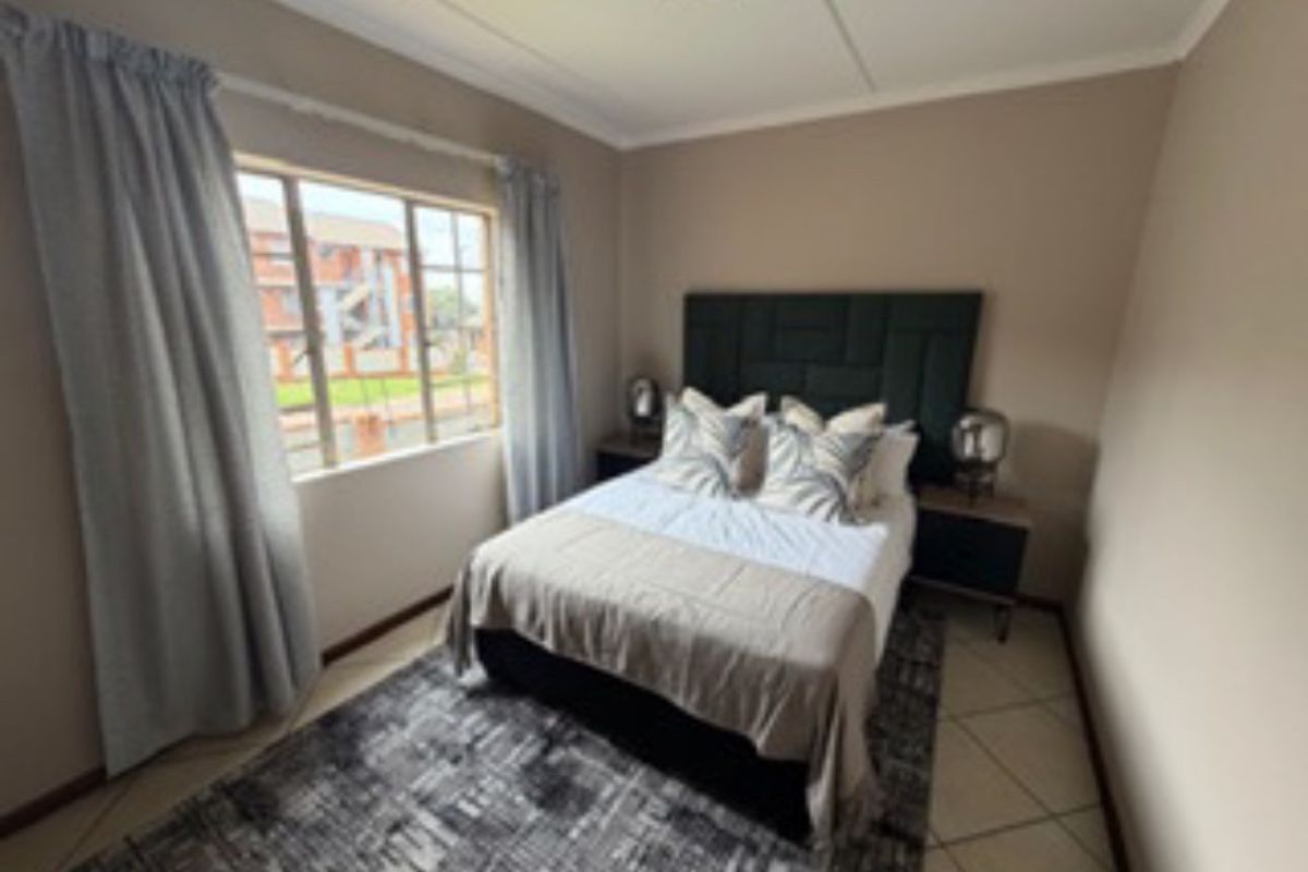 A well-lit bedroom featuring neutral wall tones, tiled flooring, and a window providing natural light.