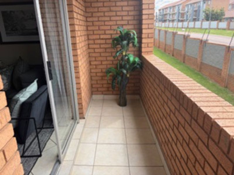 A private balcony featuring brick walls and tiled flooring, accessible via a sliding glass door, offering a view of the surrounding complex.