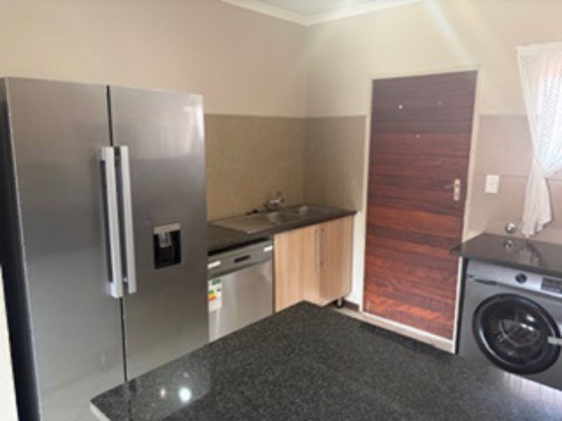 A functional kitchen area featuring granite countertops, built-in cabinetry, a stainless steel sink, and a tiled backsplash.