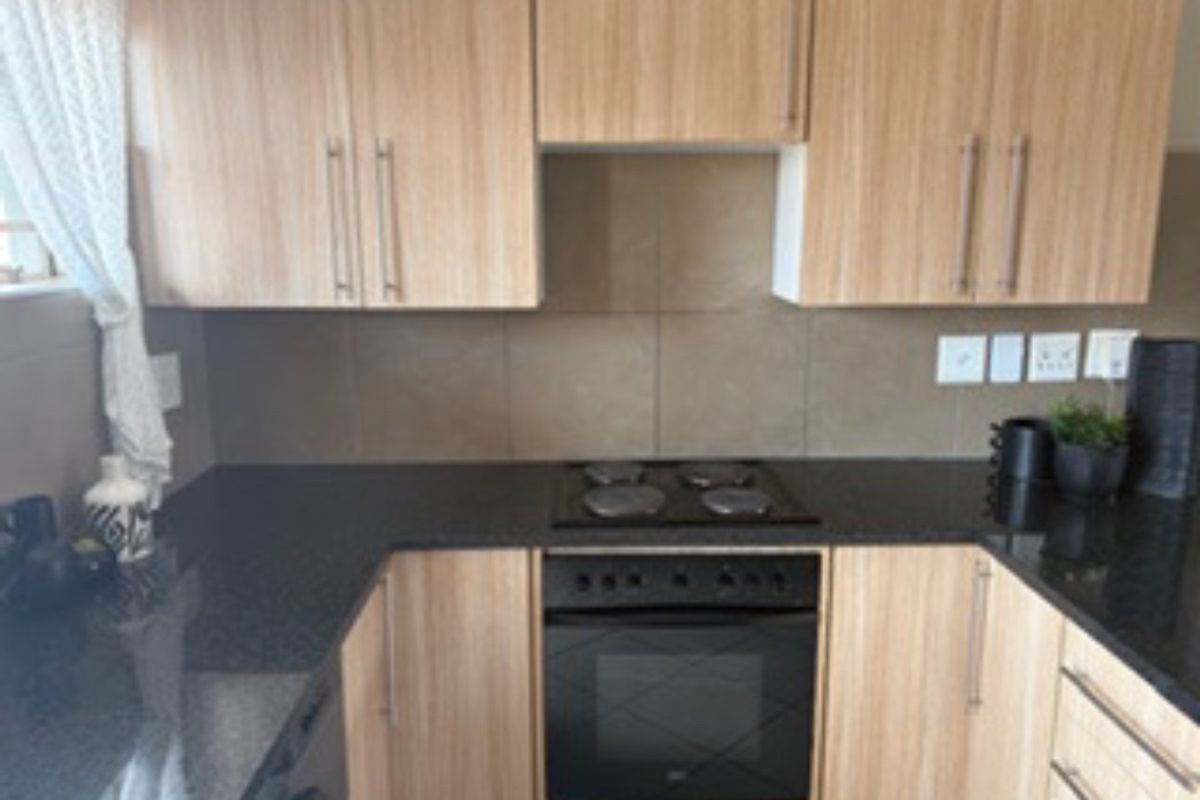 A functional kitchen featuring light wood-finish cabinetry, dark stone countertops, a tiled backsplash, and a built-in electric oven with a matching hob.