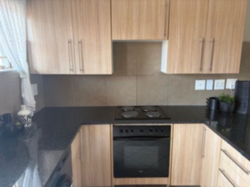 A functional kitchen featuring light wood-finish cabinetry, dark stone countertops, a tiled backsplash, and a built-in electric oven with a matching hob.