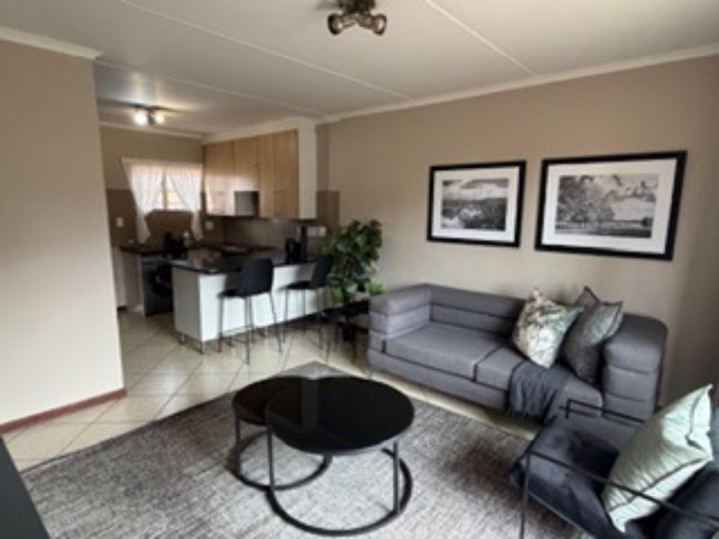 Open-plan living area featuring a functional kitchen with island seating and tiled flooring, seamlessly connected to a comfortable lounge space.