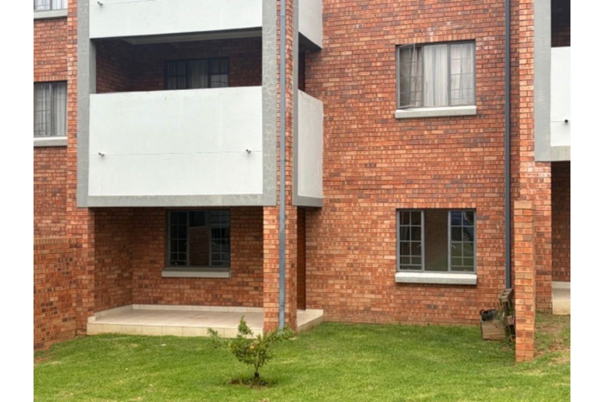 Rear view of a face brick apartment building featuring a ground floor patio and an upper-level balcony with aluminium window frames.