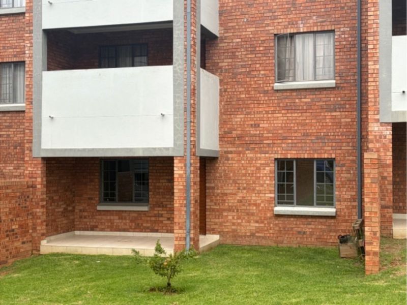 Rear view of a face brick apartment building featuring a ground floor patio and an upper-level balcony with aluminium window frames.