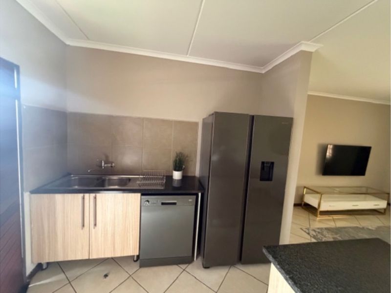 A functional kitchen area featuring light wood cabinetry, a double sink, tiled splashback, and integrated dishwasher, seamlessly flowing into the adjacent living space.