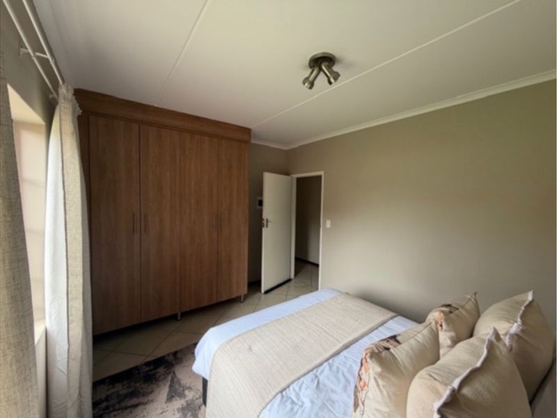 A bedroom featuring built-in wooden cupboards, tiled flooring, and a ceiling-mounted spotlight fixture.
