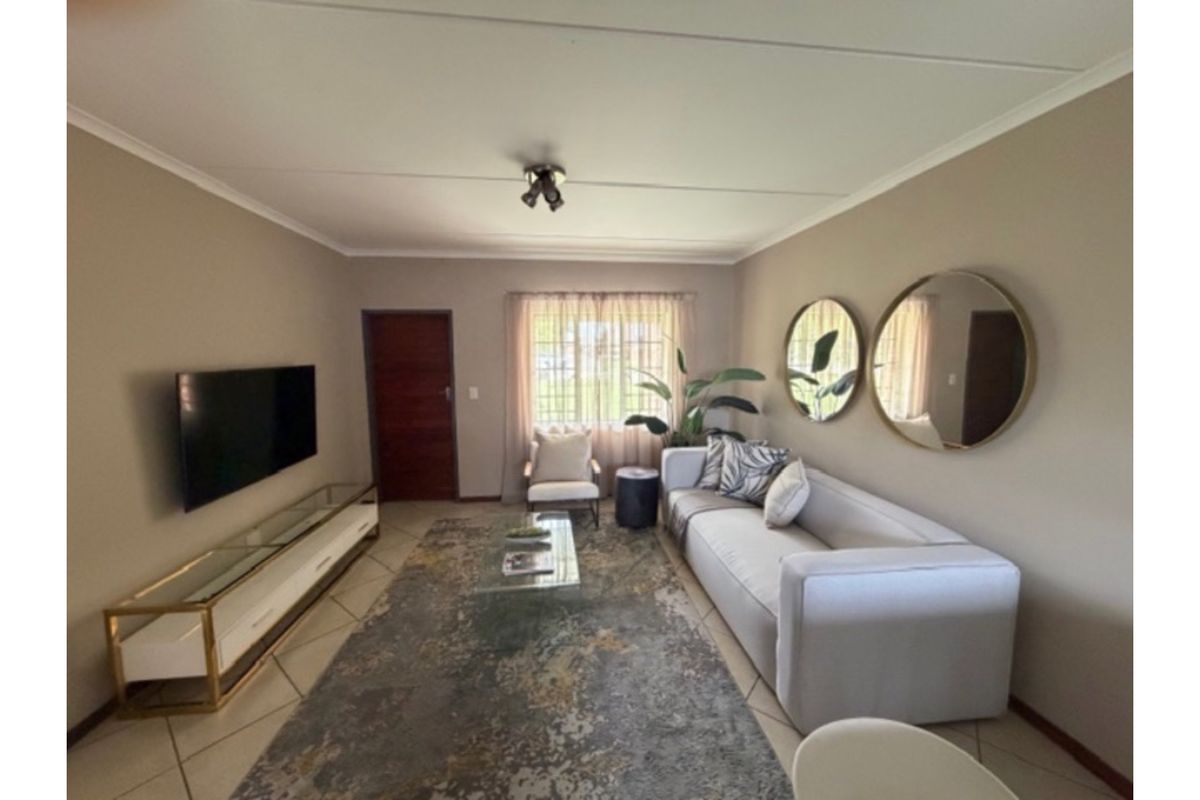 A well-maintained living room featuring neutral wall tones, tiled flooring, and a window with security bars, providing a comfortable and functional living space.