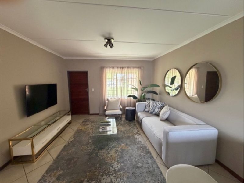 A well-maintained living room featuring neutral wall tones, tiled flooring, and a window with security bars, providing a comfortable and functional living space.