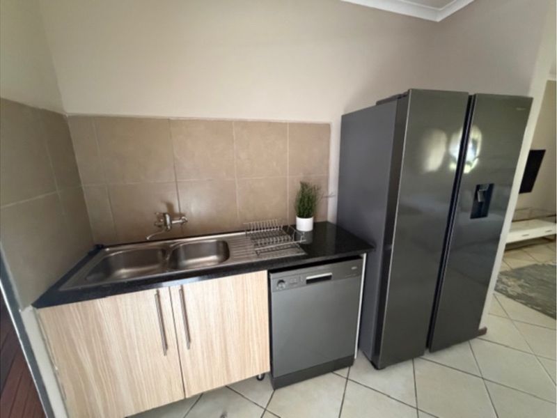 A compact kitchen area featuring a double sink, granite countertops, tiled backsplash, and integrated dishwasher, providing functional prep and wash-up space.
