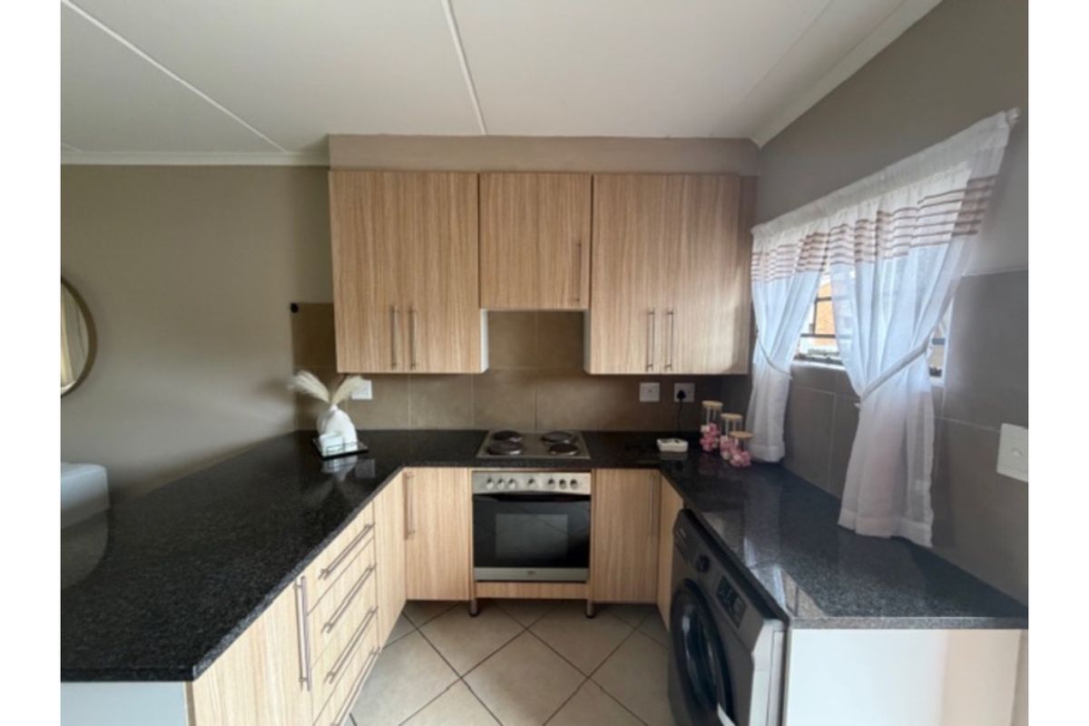 A functional kitchen featuring light wood-finish cabinetry, dark granite countertops, a built-in oven and hob, and tiled flooring.