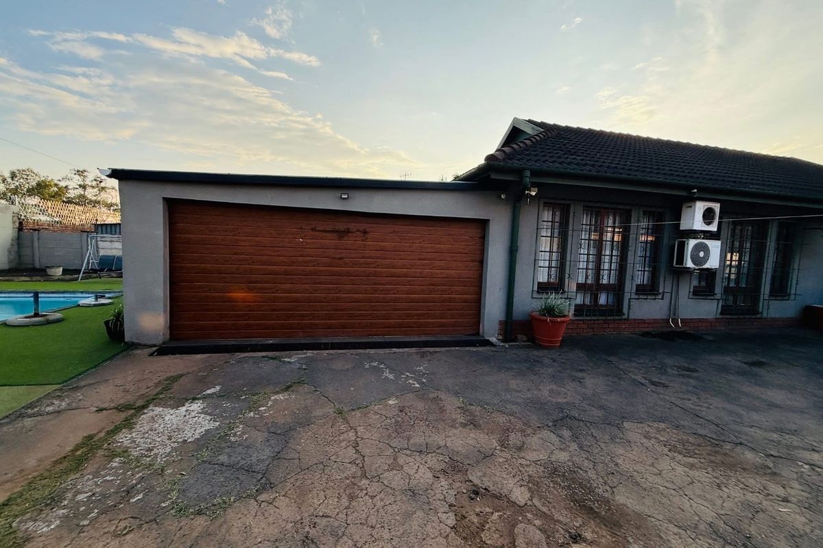 Rear exterior view featuring a garage, tiled roof, security bars on windows, external air conditioning units, and a swimming pool area.