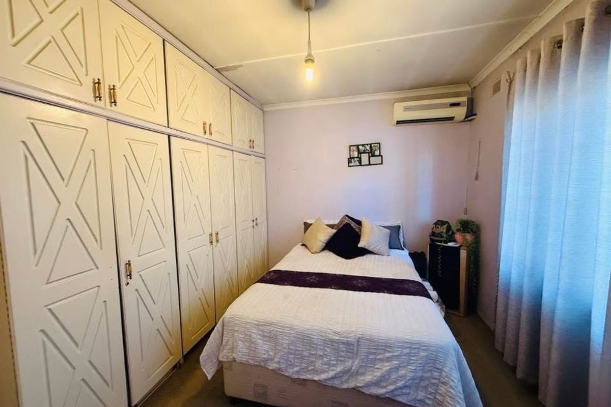 A bedroom featuring extensive built-in cabinetry, a wall-mounted air conditioning unit, and large windows with curtains.