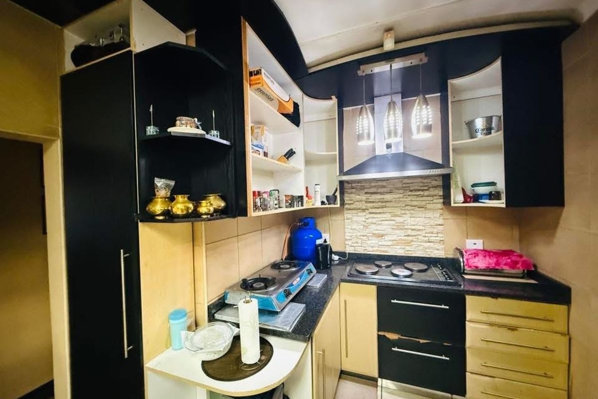 Compact kitchen featuring dark and light cabinetry, stone-look splashback, and integrated extractor fan, showing signs of wear on the cabinet doors.