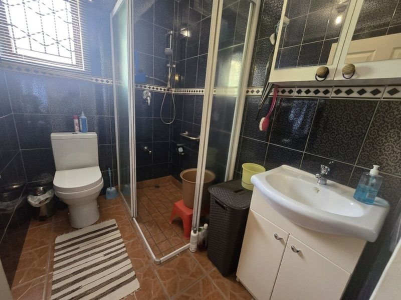 A functional bathroom featuring a shower enclosure, toilet, and vanity basin with dark tiled walls and contrasting floor tiles.