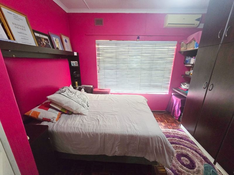 A bedroom featuring parquet flooring, built-in cupboards, and an air conditioning unit, currently finished with vibrant pink wall paint.