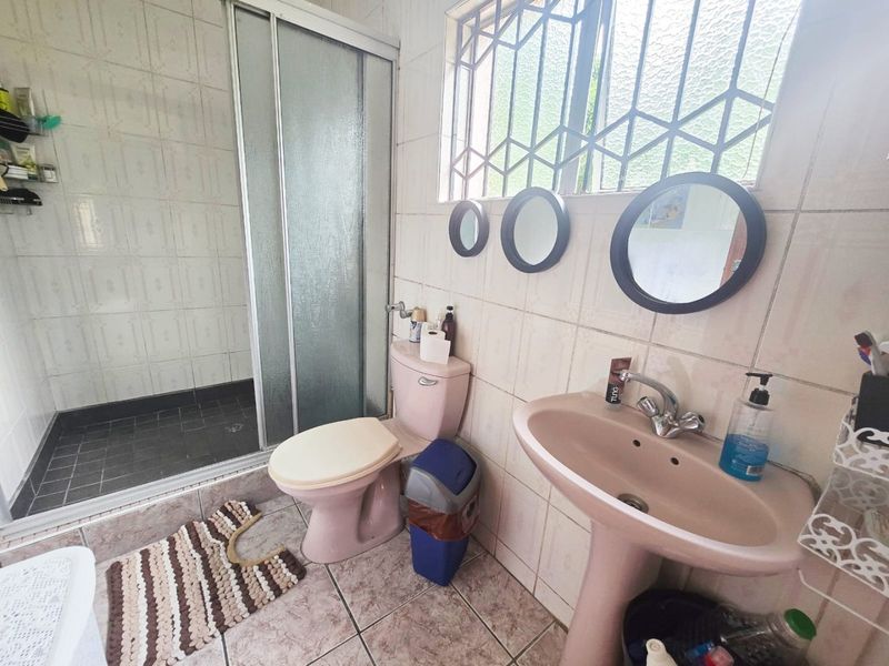 A functional bathroom featuring a pedestal basin, toilet, and a glass-enclosed shower with tiled finishes and security bars on the window.