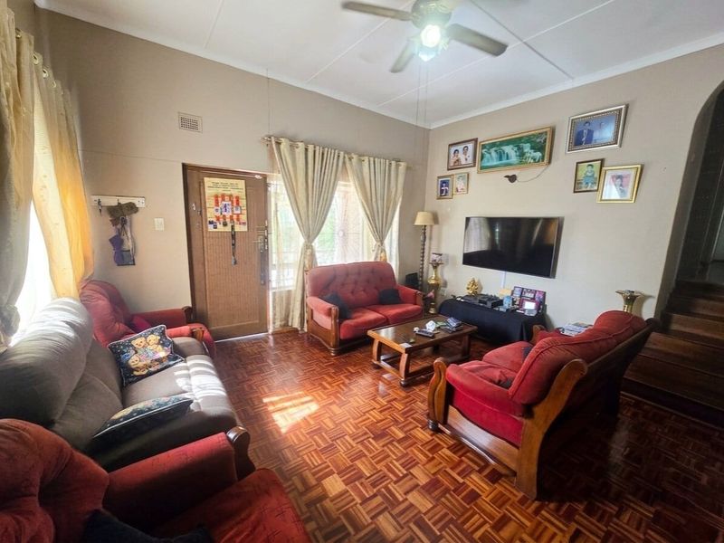 A living room featuring traditional parquet flooring, a ceiling fan, and direct access to the exterior via a timber door.