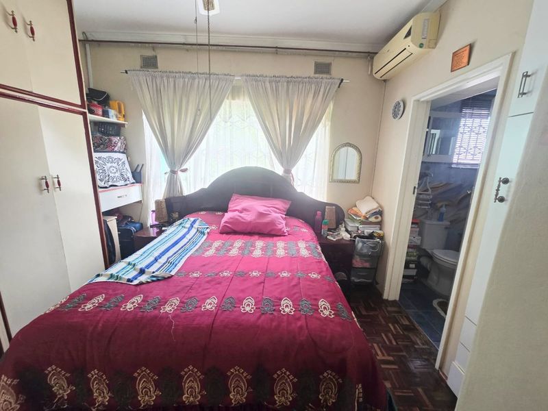 A bedroom featuring parquet flooring, built-in cupboards, and a wall-mounted air conditioning unit, with direct access to an en-suite bathroom.