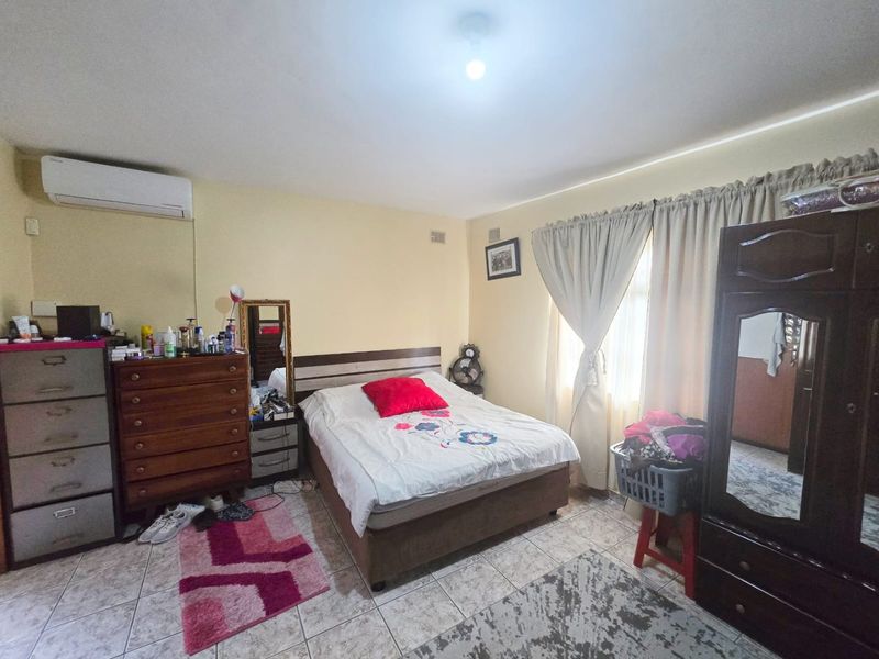 A functional bedroom featuring tiled flooring and a wall-mounted split-system air conditioner, providing a comfortable and climate-controlled living space.