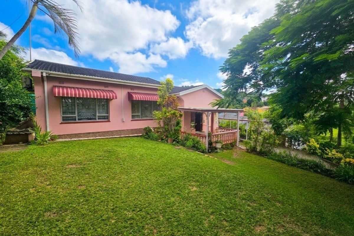 A view of the rear elevation of a pink house featuring a covered patio, security-barred windows with awnings, and a well-maintained lawn.