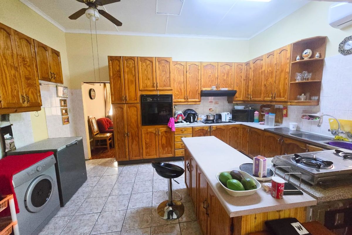 Spacious kitchen featuring extensive wooden cabinetry, a central island, built-in oven, and tiled flooring, offering a functional layout with ample storage space.