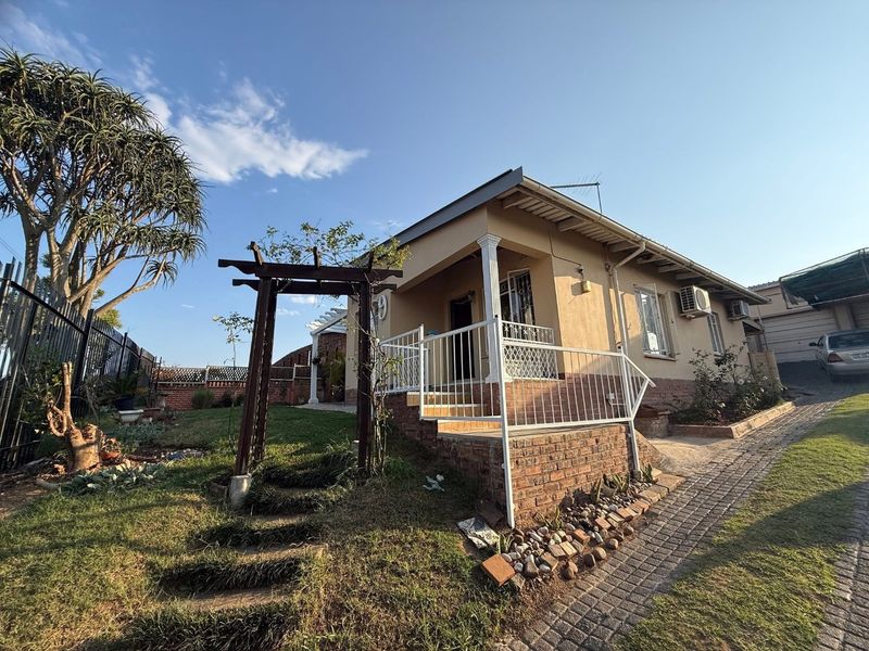 Front view of a residential house featuring a brick facade, a small pergola, and a paved driveway area.