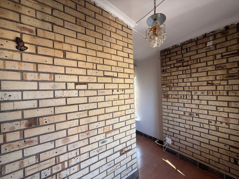 A vacant hallway featuring exposed brick walls and tiled flooring, offering a blank canvas for renovation and interior design updates.