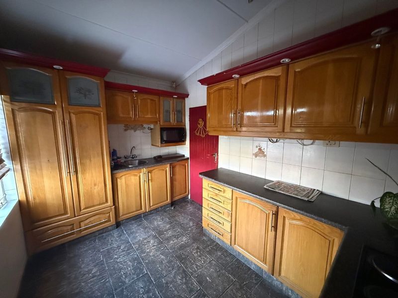 A functional kitchen featuring traditional wooden cabinetry, dark laminate countertops, tiled backsplash, and durable tiled flooring with a built-in microwave.