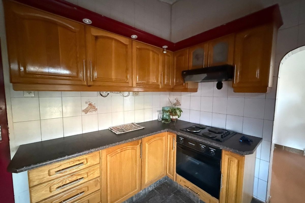 A functional kitchen featuring wooden cabinetry, built-in oven, electric hob, and tiled backsplash, offering a classic layout with potential for modern updates.