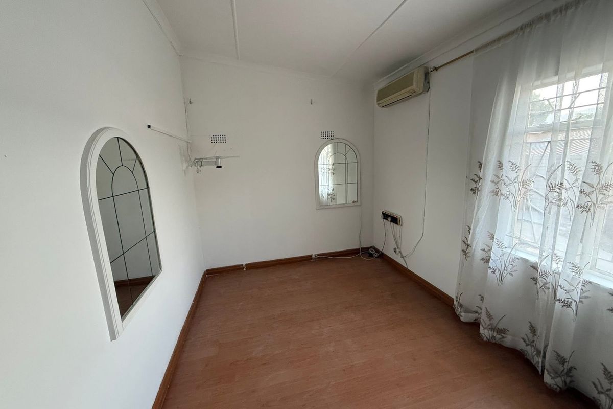 An empty bedroom featuring laminate flooring, a wall-mounted air conditioning unit, and built-in arched mirrors, offering a blank canvas for personalization.