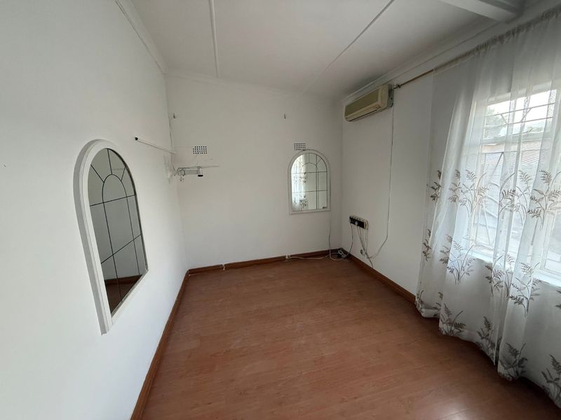 An empty bedroom featuring laminate flooring, a wall-mounted air conditioning unit, and built-in arched mirrors, offering a blank canvas for personalization.