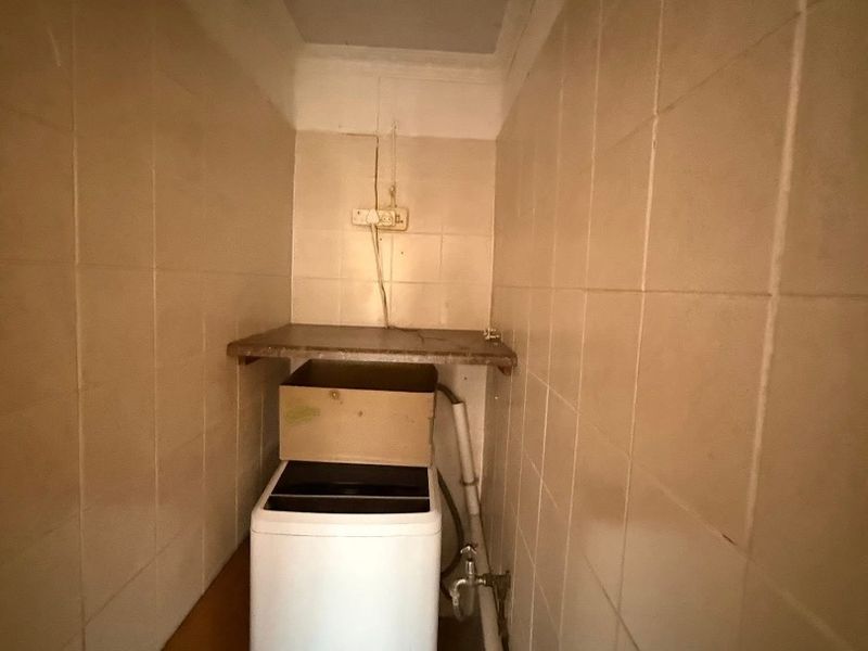 A compact laundry area featuring tiled walls and floor, with dedicated plumbing connections and a fixed shelf for utility storage.