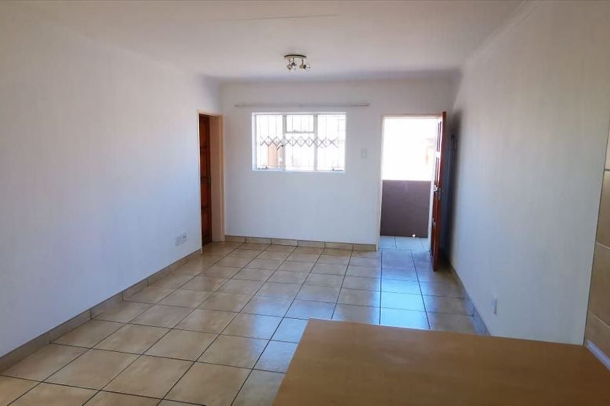 An open-plan living area featuring ceramic tiled flooring, neutral walls, and direct access to an exterior balcony through a security gate.