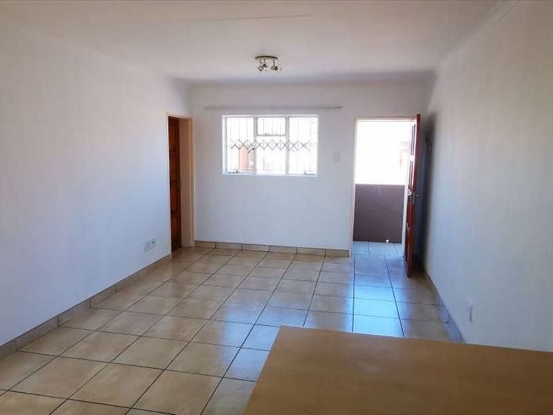 An open-plan living area featuring ceramic tiled flooring, neutral walls, and direct access to an exterior balcony through a security gate.