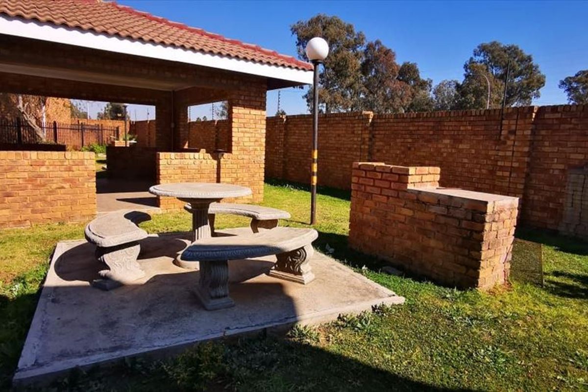 Outdoor entertainment area featuring a covered brick patio, built-in braai, concrete seating area, and a private garden enclosed by brick boundary walls.