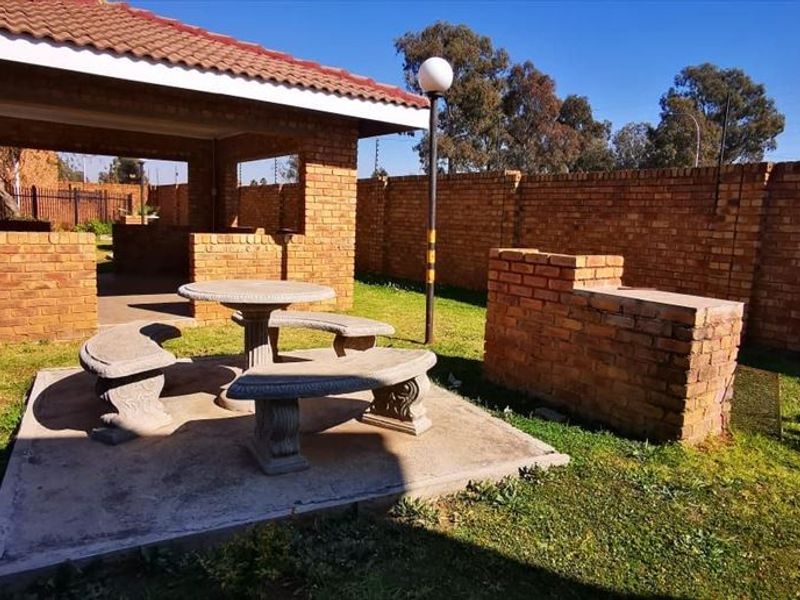 Outdoor entertainment area featuring a covered brick patio, built-in braai, concrete seating area, and a private garden enclosed by brick boundary walls.
