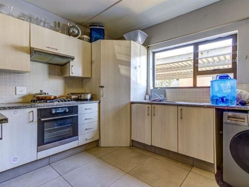 Functional kitchen featuring light wood-look cabinetry, granite countertops, built-in oven with gas hob, and tiled flooring with a window for natural light.