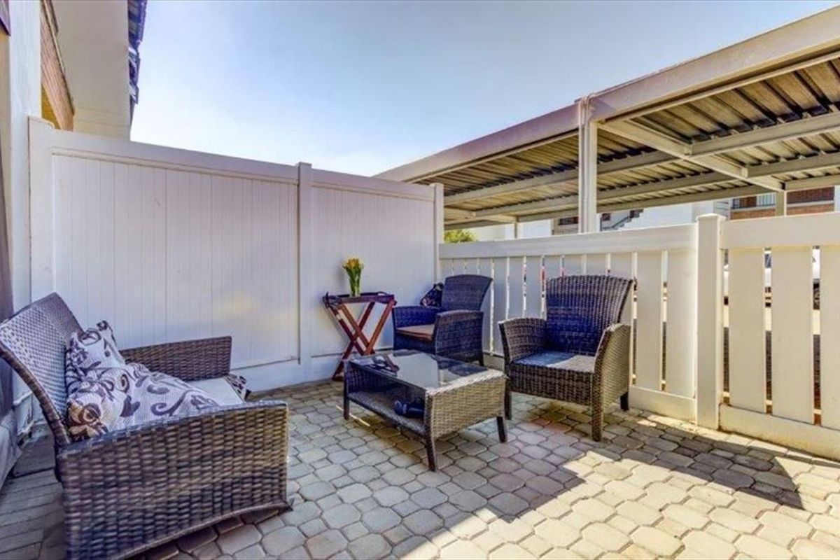 A private outdoor patio area featuring paved flooring and vinyl privacy fencing, adjacent to a covered carport structure.