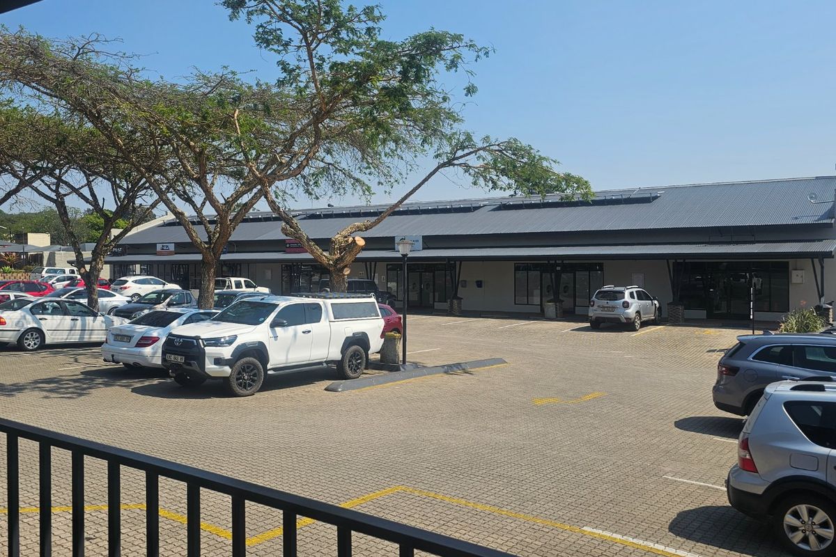 Front view of a commercial retail strip center featuring a paved parking lot, covered walkways, and solar panel installation on the roof.
