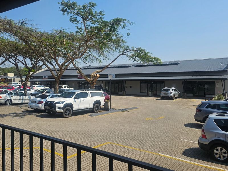 Front view of a commercial retail strip center featuring a paved parking lot, covered walkways, and solar panel installation on the roof.