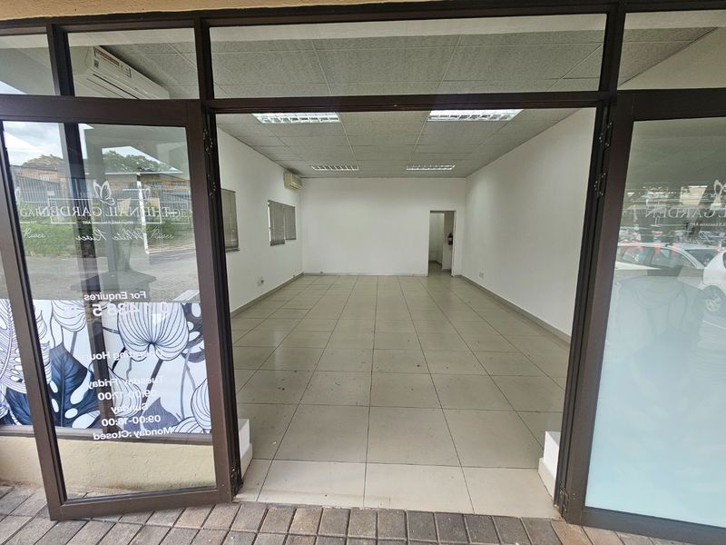 A vacant commercial entry space featuring tiled flooring, a suspended ceiling with recessed lighting, and large aluminium-framed glass doors.