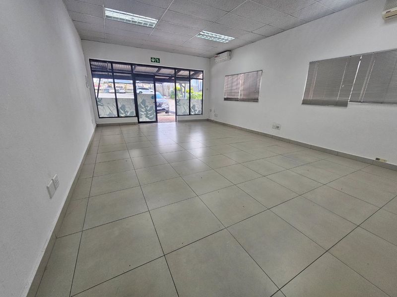 A bright, open-plan commercial office space featuring tiled flooring, a suspended ceiling with recessed lighting, and split-system air conditioning.