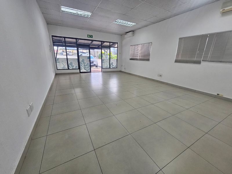 A vacant commercial office space featuring tiled flooring, a suspended ceiling with recessed lighting, air conditioning, and large glass entrance doors.