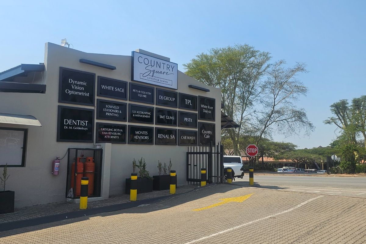 Front exterior view of Country Square Lifestyle Centre featuring a directory of commercial tenants, paved parking area, and security access gate.
