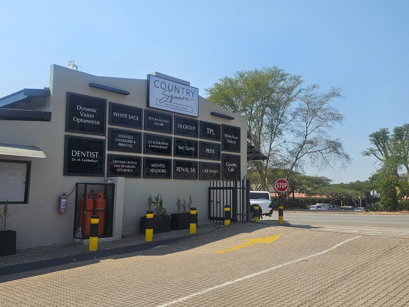 Front exterior view of Country Square Lifestyle Centre featuring a directory of commercial tenants, paved parking area, and security access gate.